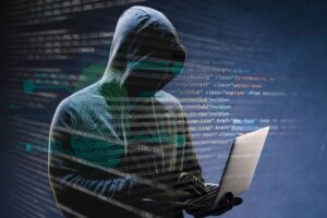 Persona encapuchada manipulando una laptop, rodeada de líneas de código y huellas digitales, simbolizando la actividad de un ciberdelincuente en un ataque de ransomware